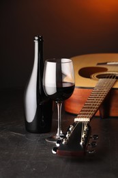 Photo of Acoustic guitar and red wine on black table with brown light, closeup