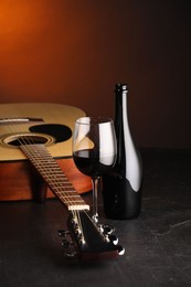 Photo of Acoustic guitar and red wine on black table with brown light, closeup