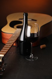 Photo of Acoustic guitar and red wine on black table with brown light, closeup