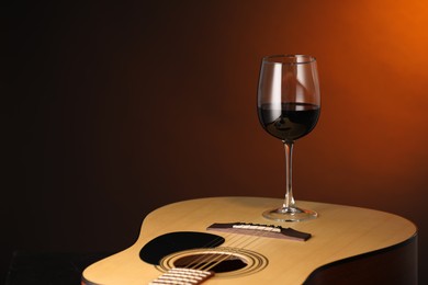 Photo of Acoustic guitar and red wine on brown background, closeup. Space for text