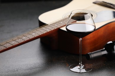 Photo of Acoustic guitar and red wine on black table, closeup