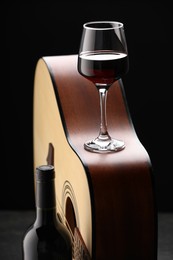 Photo of Acoustic guitar and red wine on black table, closeup