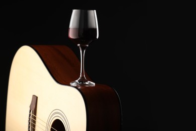 Photo of Acoustic guitar and red wine on black background, closeup. Space for text