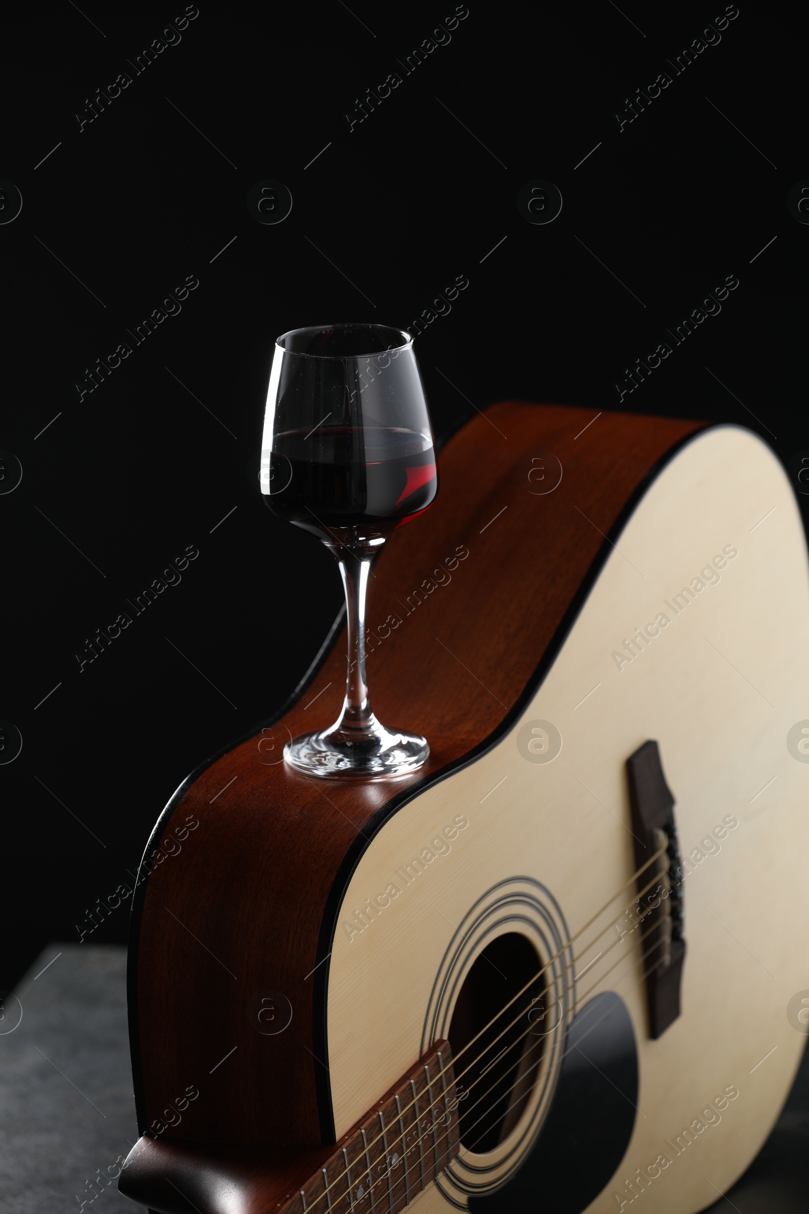 Acoustic guitar and red wine on black table, closeup Photo of Acoustic guitar and red wine on black table, closeup