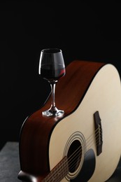 Photo of Acoustic guitar and red wine on black table, closeup