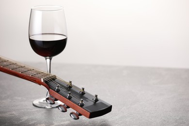 Photo of Acoustic guitar and red wine on grey table against white background, closeup. Space for text