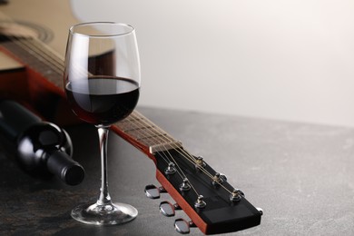 Photo of Acoustic guitar and red wine on grey table against white background, closeup. Space for text