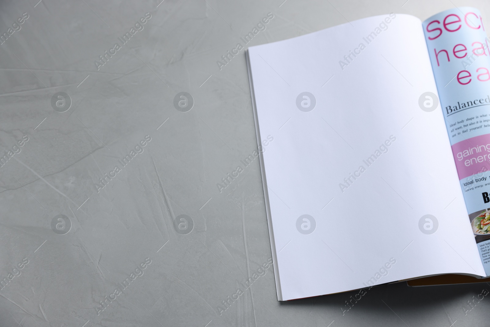Photo of Open magazine on light grey table. Mockup for design