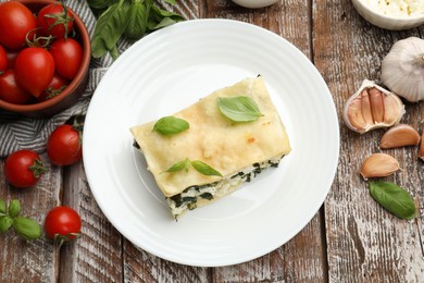 Photo of Piece of tasty vegetarian lasagna and ingredients on wooden table, flat lay