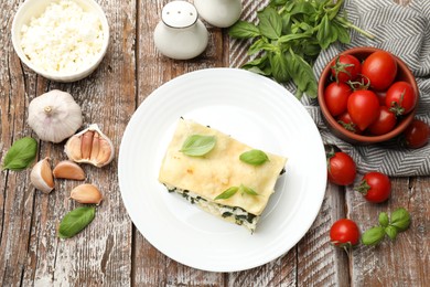 Photo of Piece of tasty vegetarian lasagna and ingredients on wooden table, flat lay