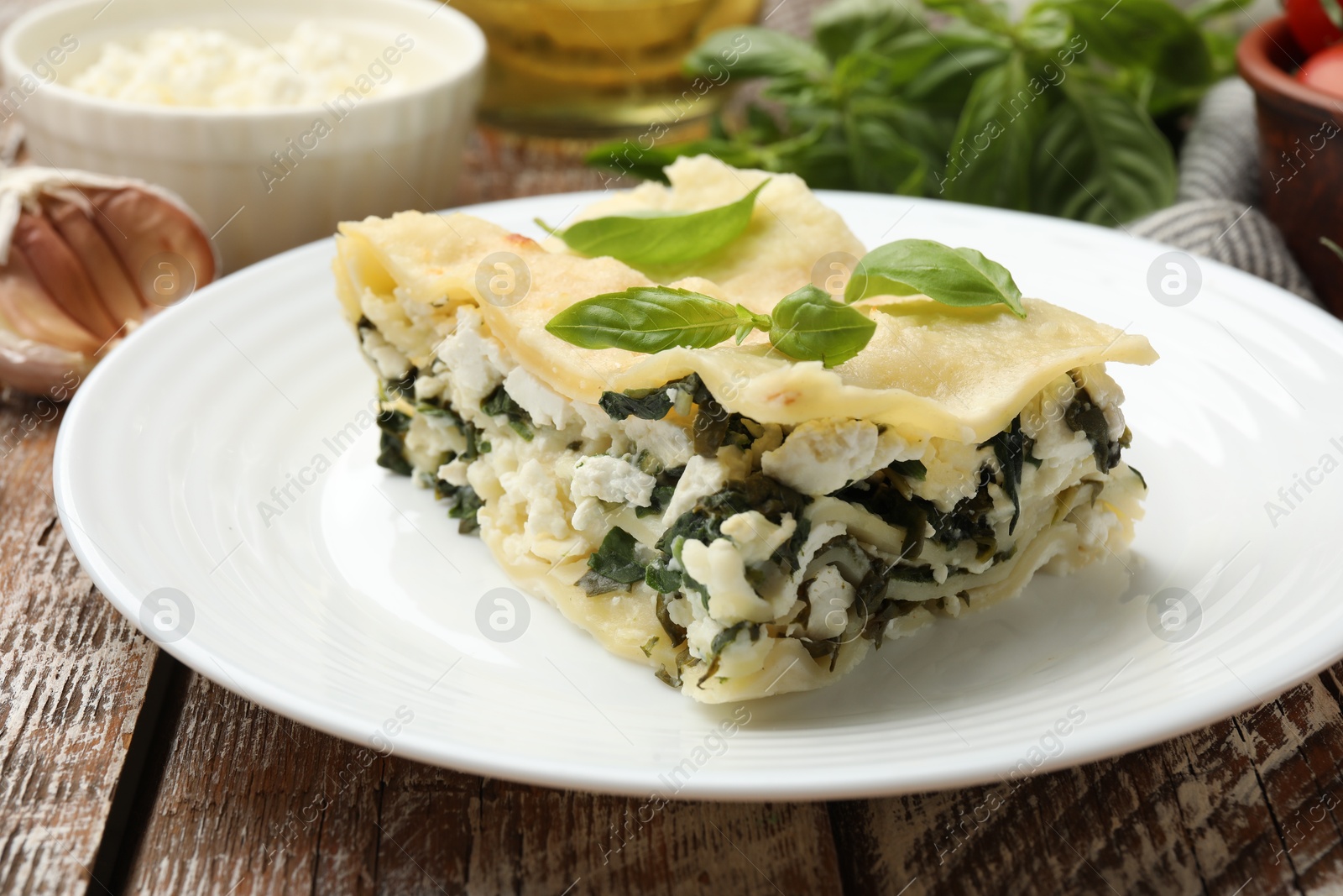 Photo of Piece of tasty vegetarian lasagna and ingredients on wooden table, closeup