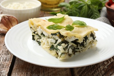 Photo of Piece of tasty vegetarian lasagna and ingredients on wooden table, closeup