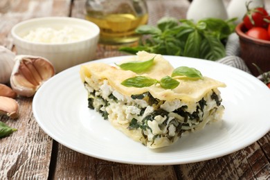 Photo of Piece of tasty vegetarian lasagna and ingredients on wooden table, closeup