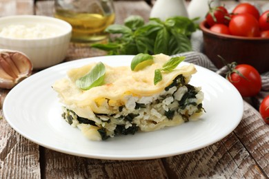 Photo of Piece of tasty vegetarian lasagna and ingredients on wooden table, closeup