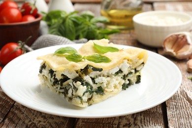 Photo of Piece of tasty vegetarian lasagna and ingredients on wooden table, closeup