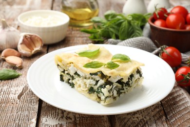 Photo of Piece of tasty vegetarian lasagna and ingredients on wooden table, closeup
