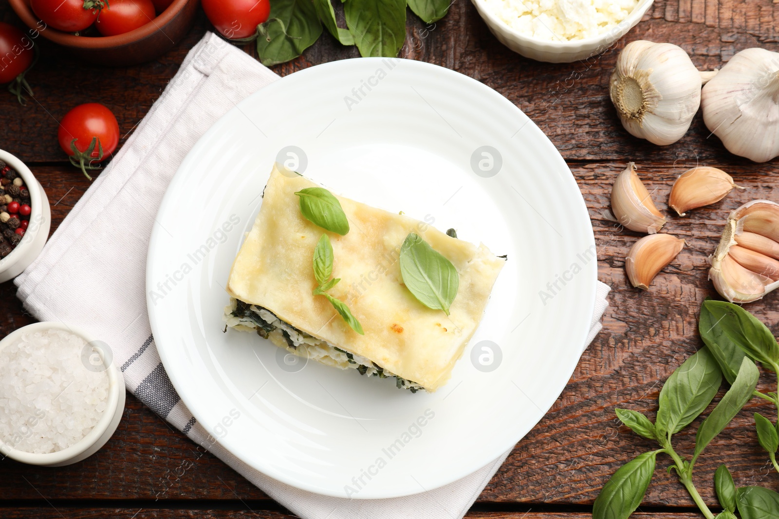 Photo of Piece of tasty vegetarian lasagna and ingredients on wooden table, flat lay