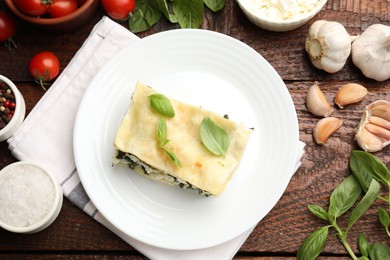 Photo of Piece of tasty vegetarian lasagna and ingredients on wooden table, flat lay
