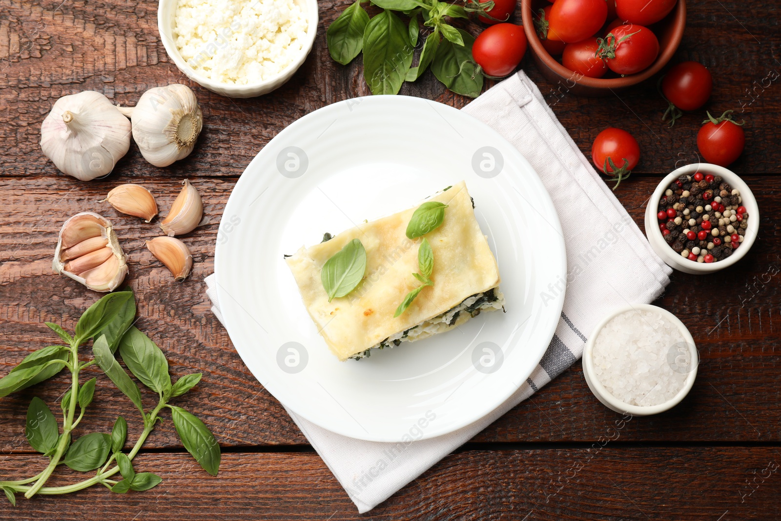 Photo of Piece of tasty vegetarian lasagna and ingredients on wooden table, flat lay
