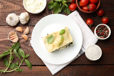 Photo of Piece of tasty vegetarian lasagna and ingredients on wooden table, flat lay