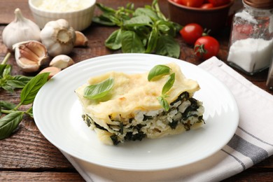 Photo of Piece of tasty vegetarian lasagna and ingredients on wooden table, closeup