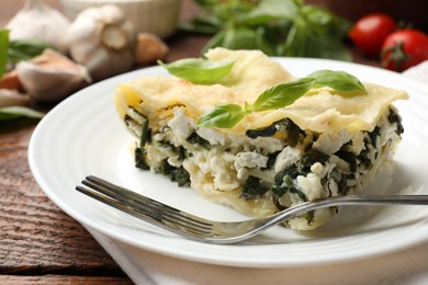 Photo of Piece of tasty vegetarian lasagna and ingredients on wooden table, closeup
