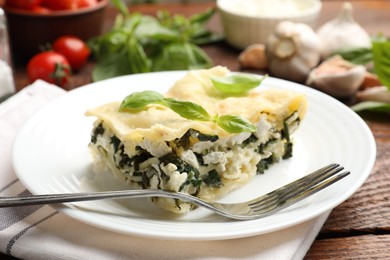 Photo of Piece of tasty vegetarian lasagna and ingredients on wooden table, closeup