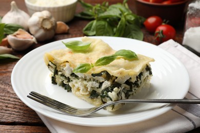 Photo of Piece of tasty vegetarian lasagna and ingredients on wooden table, closeup
