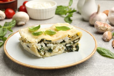 Photo of Piece of tasty vegetarian lasagna and ingredients on grey table, closeup