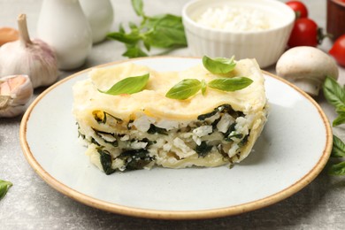 Photo of Piece of tasty vegetarian lasagna and ingredients on grey table, closeup