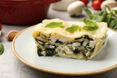 Photo of Piece of tasty vegetarian lasagna and ingredients on grey table, closeup