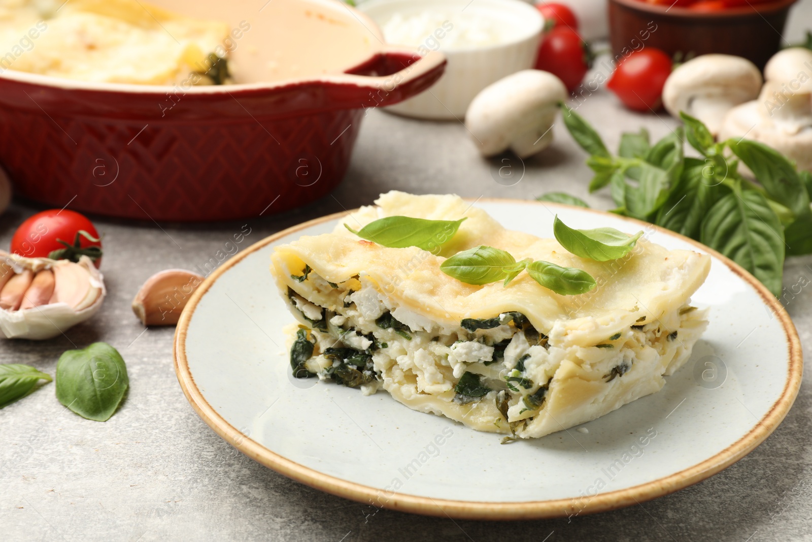 Photo of Piece of tasty vegetarian lasagna and ingredients on grey table, closeup