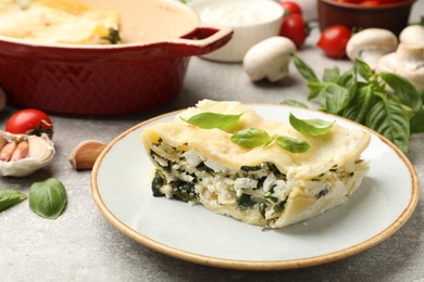 Photo of Piece of tasty vegetarian lasagna and ingredients on grey table, closeup