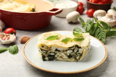 Photo of Piece of tasty vegetarian lasagna and ingredients on grey table, closeup