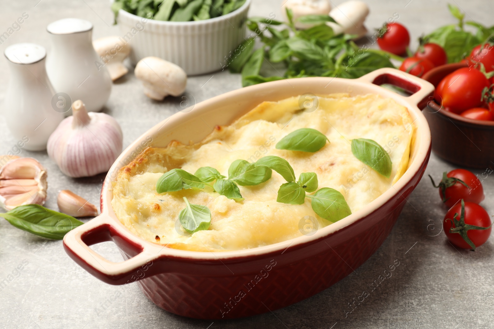 Photo of Tasty vegetarian lasagna and ingredients on grey table, closeup