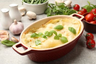 Photo of Tasty vegetarian lasagna and ingredients on grey table, closeup