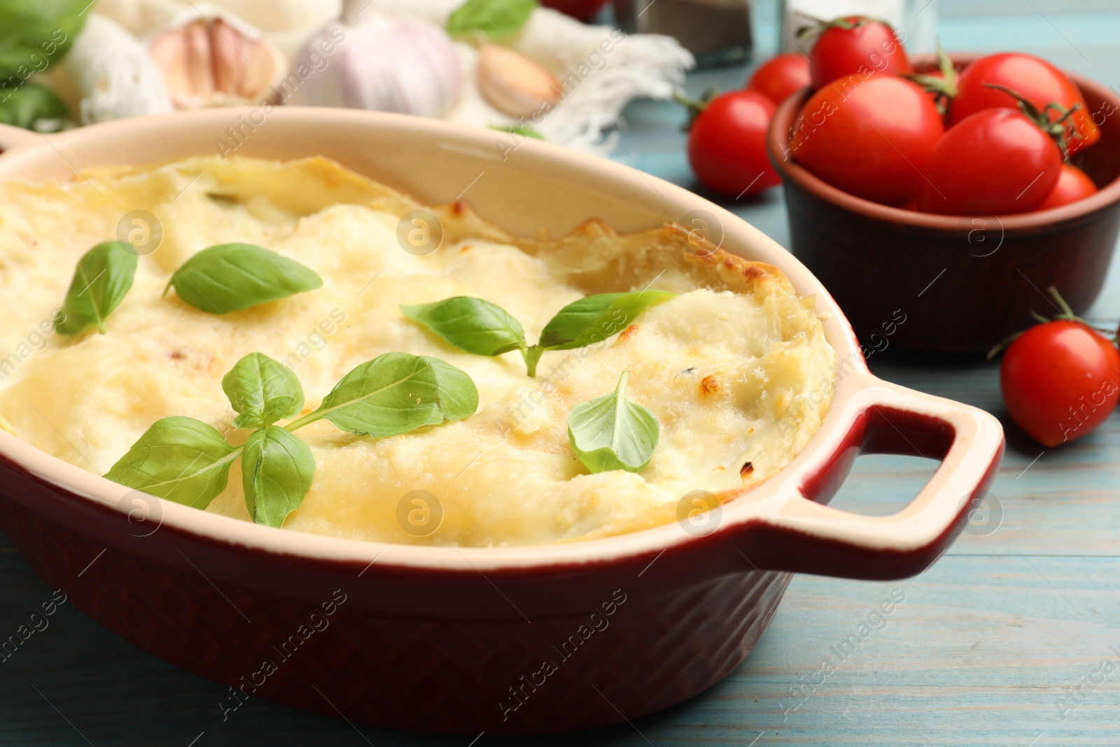 Photo of Tasty vegetarian lasagna and ingredients on light blue wooden table, closeup