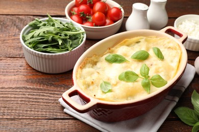 Photo of Tasty vegetarian lasagna and ingredients on wooden table, closeup