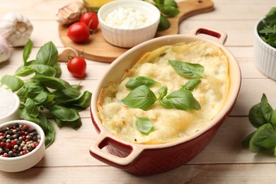 Photo of Tasty vegetarian lasagna and ingredients on wooden table, closeup