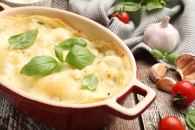 Photo of Tasty vegetarian lasagna and ingredients on wooden table, closeup