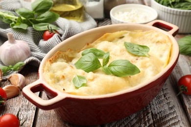 Photo of Tasty vegetarian lasagna and ingredients on wooden table, closeup