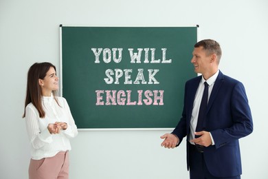 Image of Teacher and student near green chalkboard with text You Will Speak English. Language course