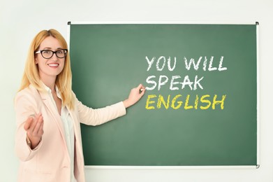 Image of Teacher pointing at text You Will Speak English on green chalkboard. Language course