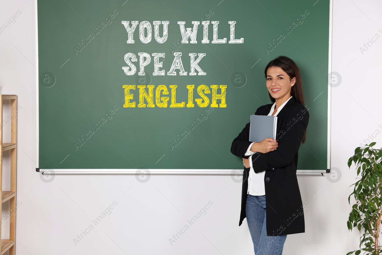 Teacher near green chalkboard with text You Will Speak English in classroom. Language course Image of Teacher near green chalkboard with text You Will Speak English in classroom. Language course