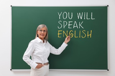 Image of Teacher pointing at text You Will Speak English on green chalkboard. Language course