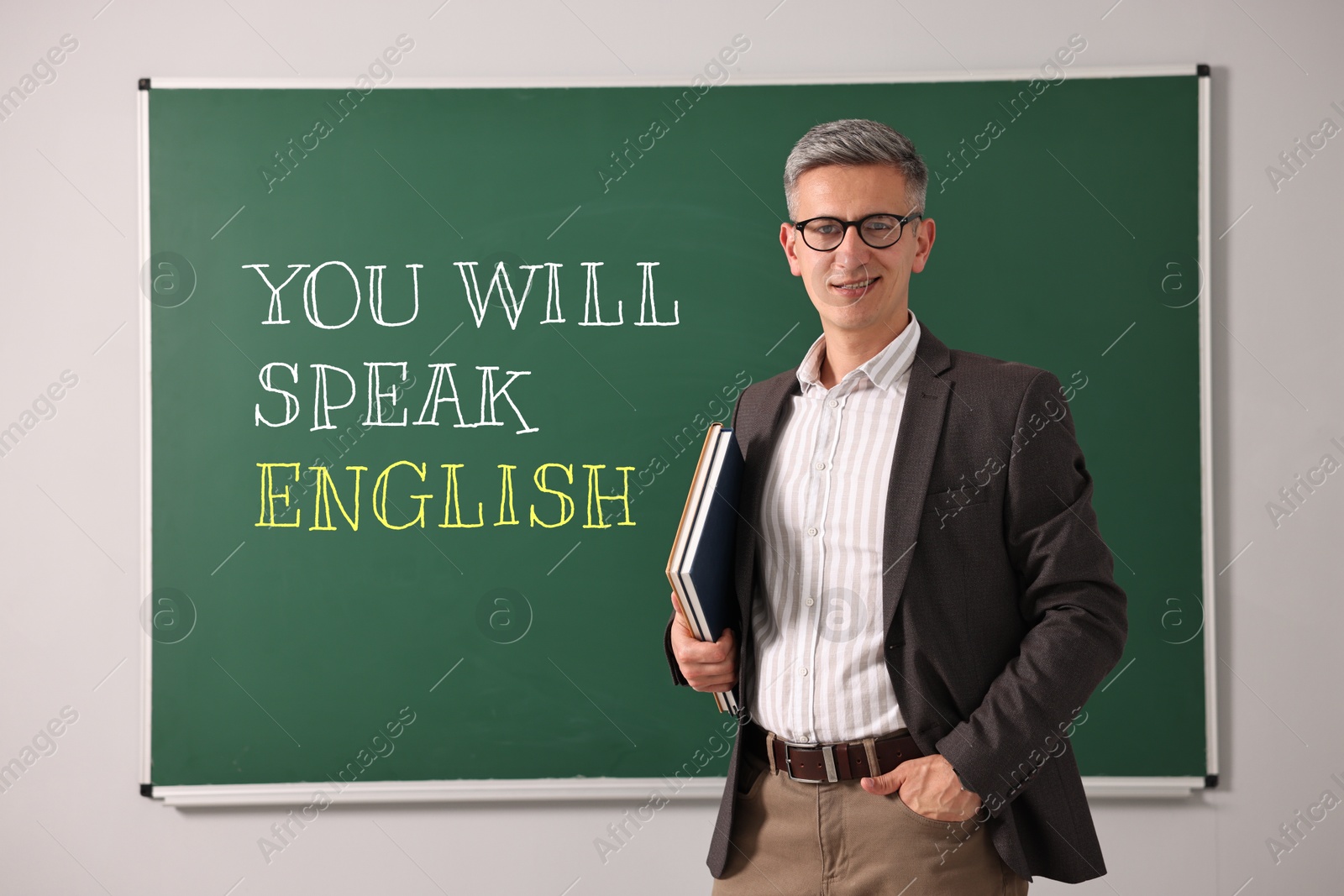 Teacher near green chalkboard with text You Will Speak English. Language course Image of Teacher near green chalkboard with text You Will Speak English. Language course