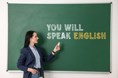 Image of Teacher pointing at text You Will Speak English on green chalkboard. Language course