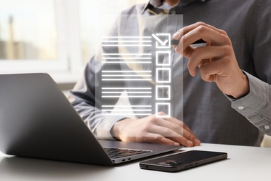 Image of Man putting tick in check list on virtual screen at table with laptop and mobile phone, closeup