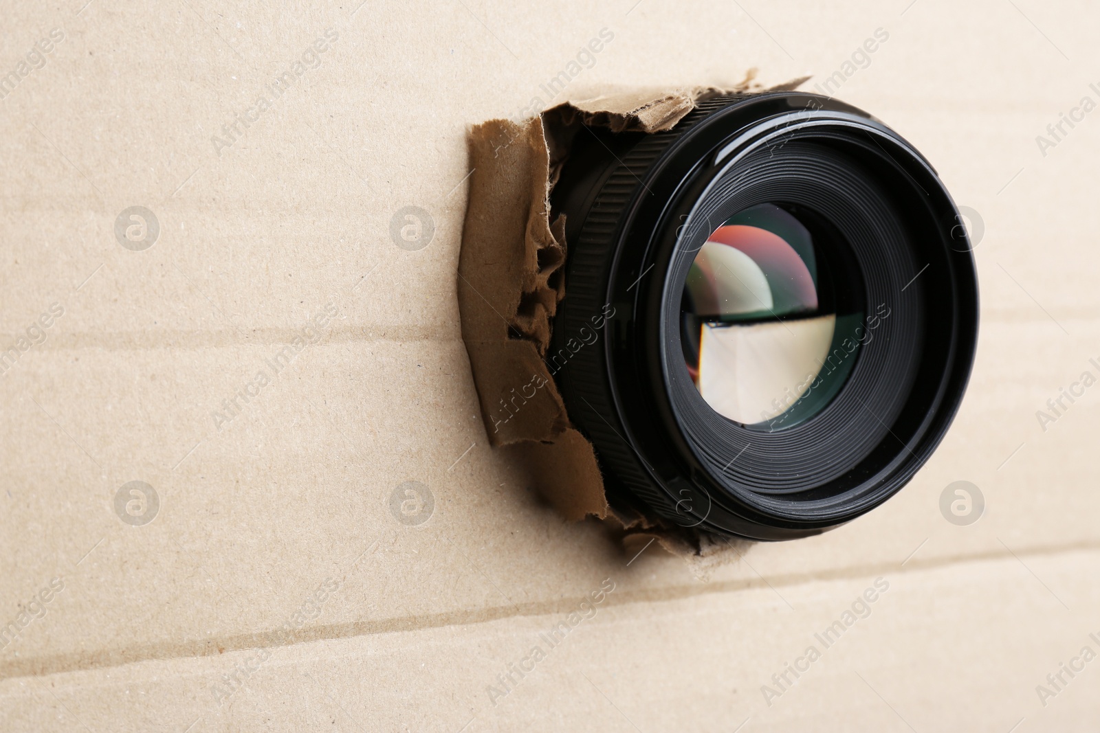 Hidden camera lens through hole in cardboard, closeup. Space for text Photo of Hidden camera lens through hole in cardboard, closeup. Space for text
