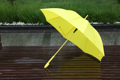 Photo of One yellow umbrella on wet bench outdoors